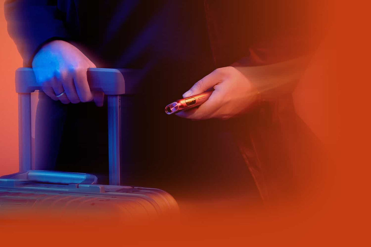 A person holding the handle of a suitcase with one hand and an electronic cigarette in the other, surrounded by an orange and blue colored lighting effect.