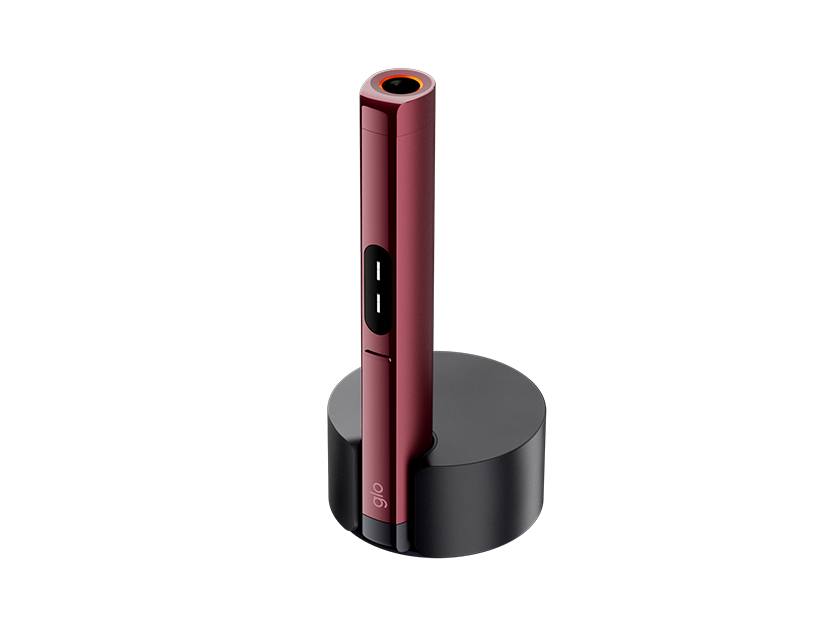 A sleek, red cylindrical electronic device with a black button sits upright in a round black charging dock against a plain white background.